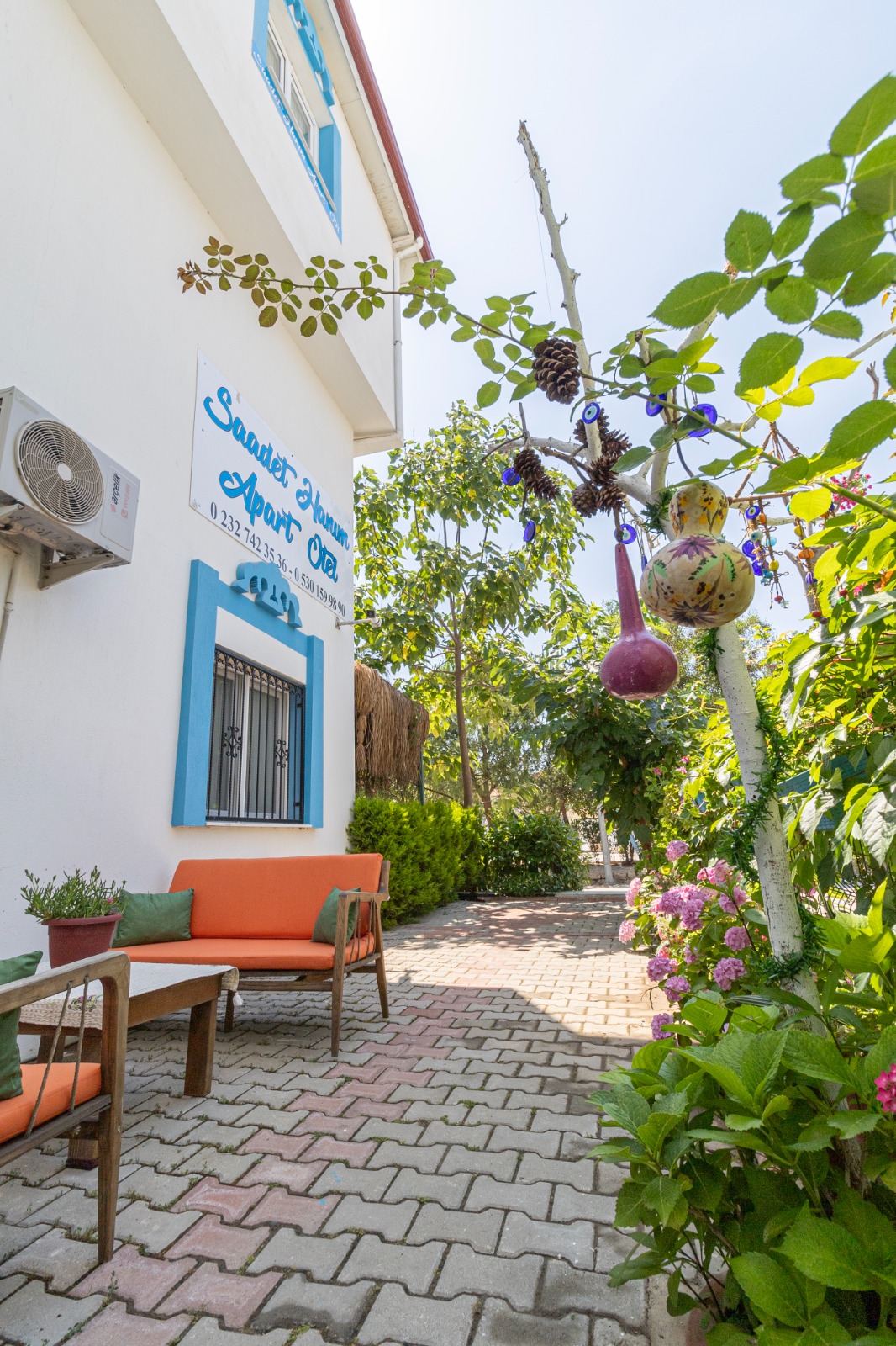 Ürkmez Apart otel bahçesi - Gölgelikli oturma alanları ve çiçeklerle çevrili huzurlu ortam